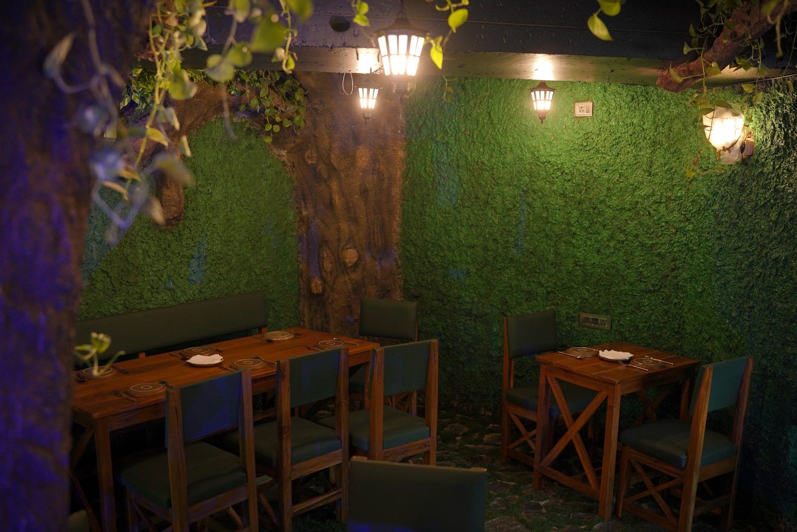 Booth seating under a giant tree with moss walls and lanterns