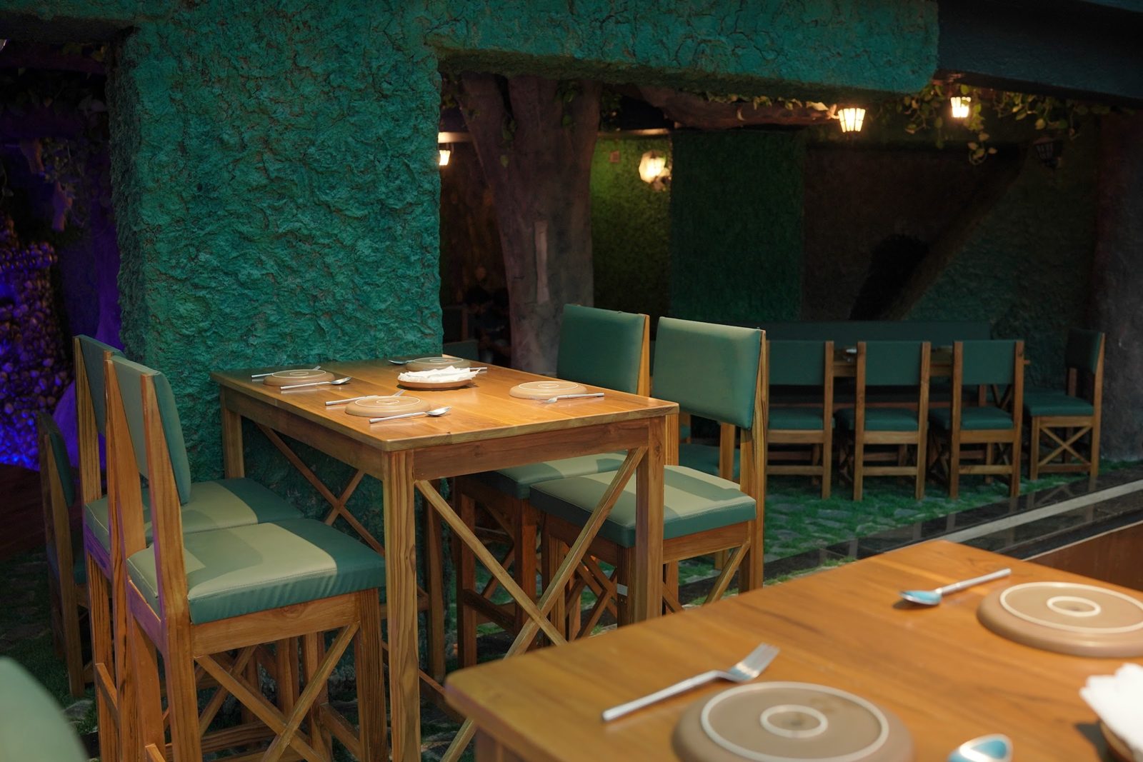 Dining tables under a giant tree with lanterns and moss walls at Forest Rogue Brews